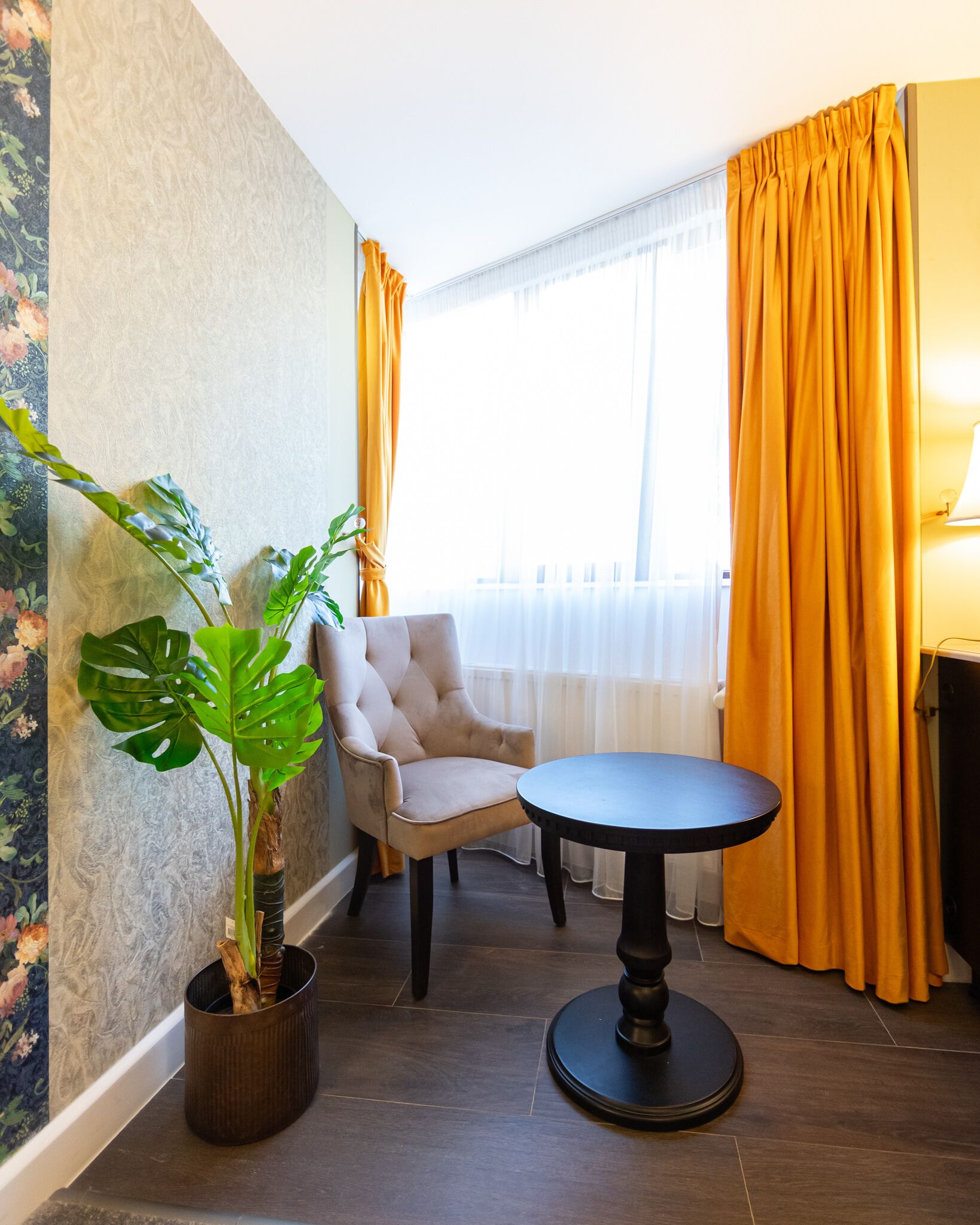 A room with a round table, a chair, a potted plant, and curtains.