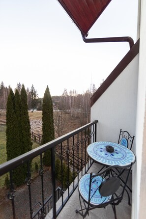 A balcony with two blue and white patterned tables and chairs, a metal railing, and a view of a park with trees and a building in the distance. - Torres Poiana (Brasov)