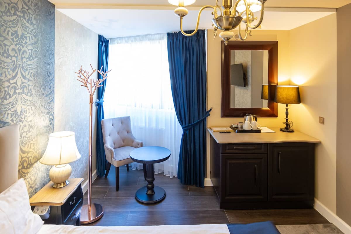 Ein Hotelzimmer mit einem Bett, einem Schreibtisch, einem Sessel, einem Schminktisch mit Spiegel und zwei Lampen.