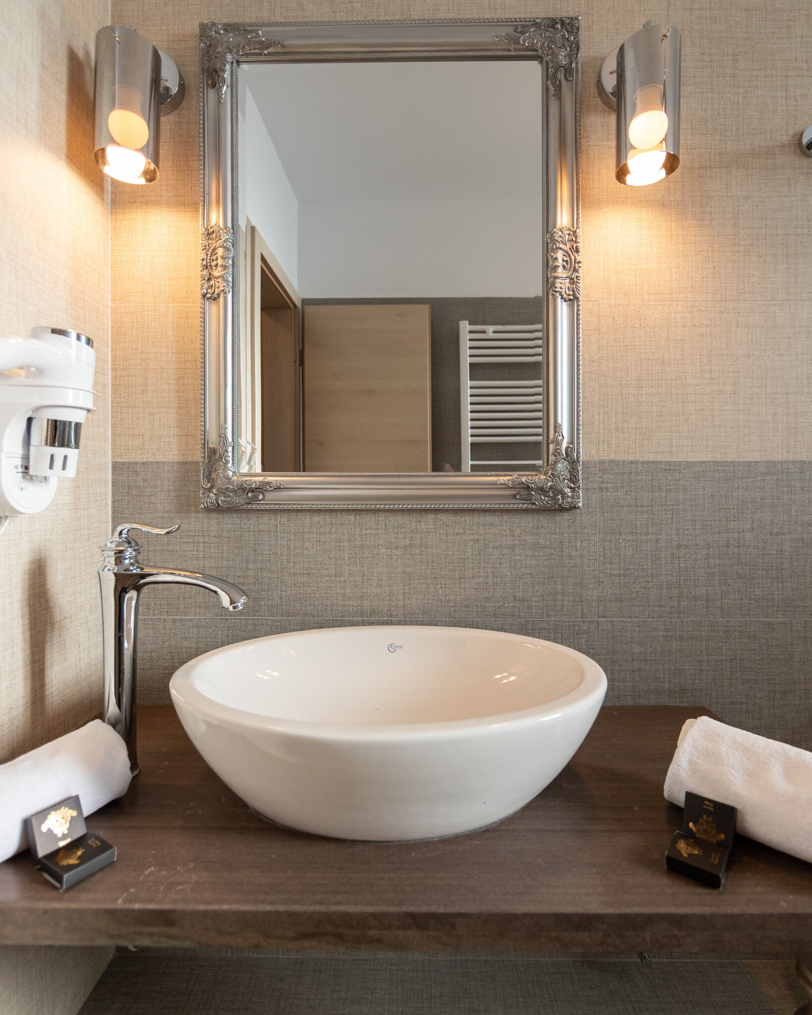 A bathroom with a large oval sink, a mirror with ornate detailing, and wall-mounted lighting.