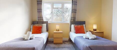 A double room with two beds, each with a nightstand, a window with curtains, and a view of trees outside.