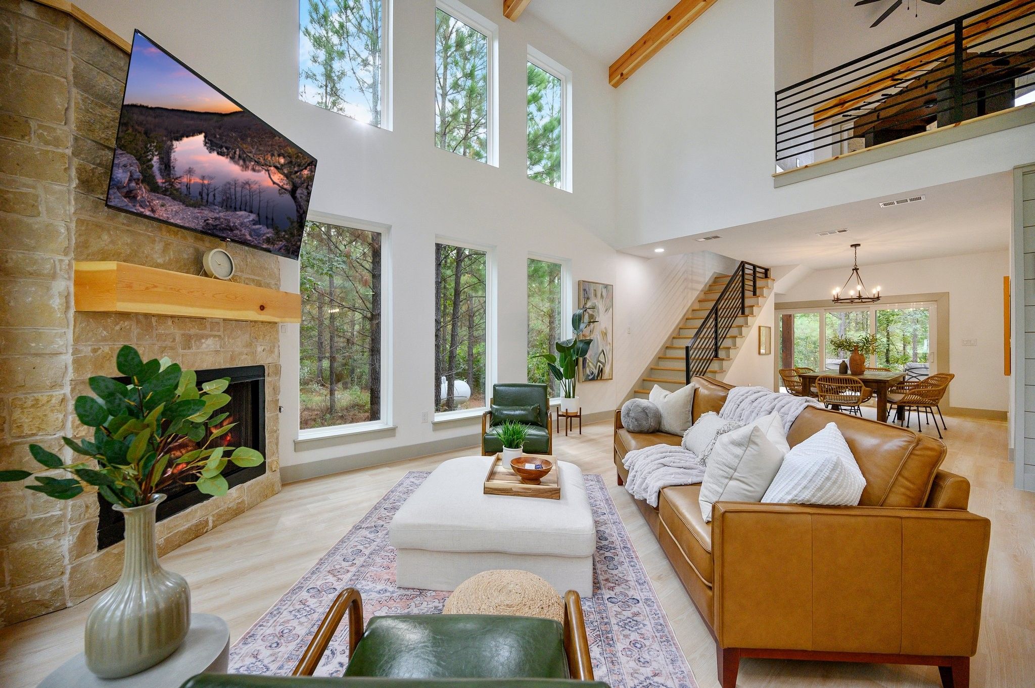 A spacious living room with a fireplace, large windows, a staircase, and a dining area.