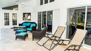 A spacious patio with a ceiling fan, a sofa with teal cushions, and lounge chairs. - Family Vacation Home in Fort Myers (Lee County)