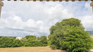 Vista desde un balcón techado con vistas a un área verde con árboles y un edificio a lo lejos.