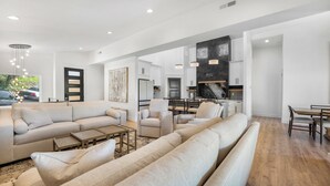 A spacious living room with a large sectional sofa, a dining area with a wooden table, and a kitchen with dark countertops. - Modern Lake Escape: Pool, Spa, Dock, Game Room, Mini Golf, Sleeps 29! (Lake Ozark)