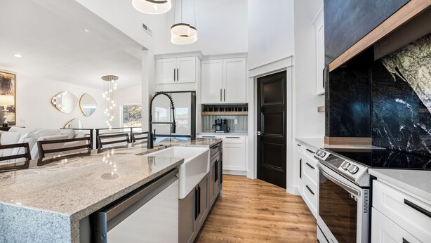A modern kitchen with white cabinetry, a granite countertop, and a black marble backsplash. - Modern Lake Escape: Pool, Spa, Dock, Game Room, Mini Golf, Sleeps 29! (Lake Ozark)