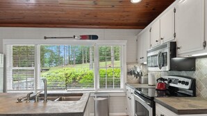 Una cocina con un ventanal grande, techo de madera y armarios blancos.