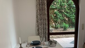 Ein Essbereich mit Tisch für zwei Personen, ein Fenster mit Blick auf Bäume und eine Tür, die nach draußen führt.