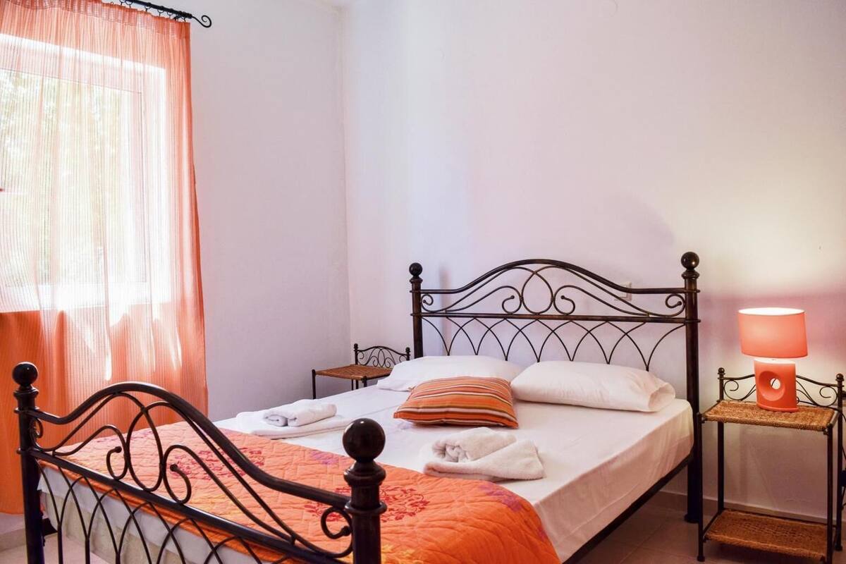 A neatly made bed with a headboard, a bedside table with a lamp, and a window with sheer curtains.