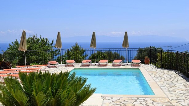 A pool with lounge chairs and umbrellas, surrounded by greenery and a clear view of the sea. - Ostria's House (Kefalonia)