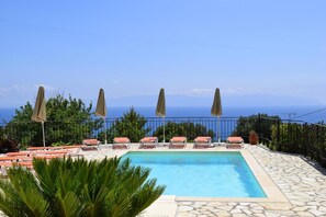 A pool with lounge chairs and umbrellas, surrounded by greenery and a clear view of the sea. - Ostria's House (Kefalonia)