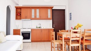 A compact kitchen with wooden cabinets, a white stove, and a dining area with a wooden table and chairs. - Ostria's House (Kefalonia)