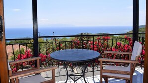 A balcony with a round table and two chairs, overlooking a scenic view of the sea and lush greenery. - Ostria's House (Kefalonia)