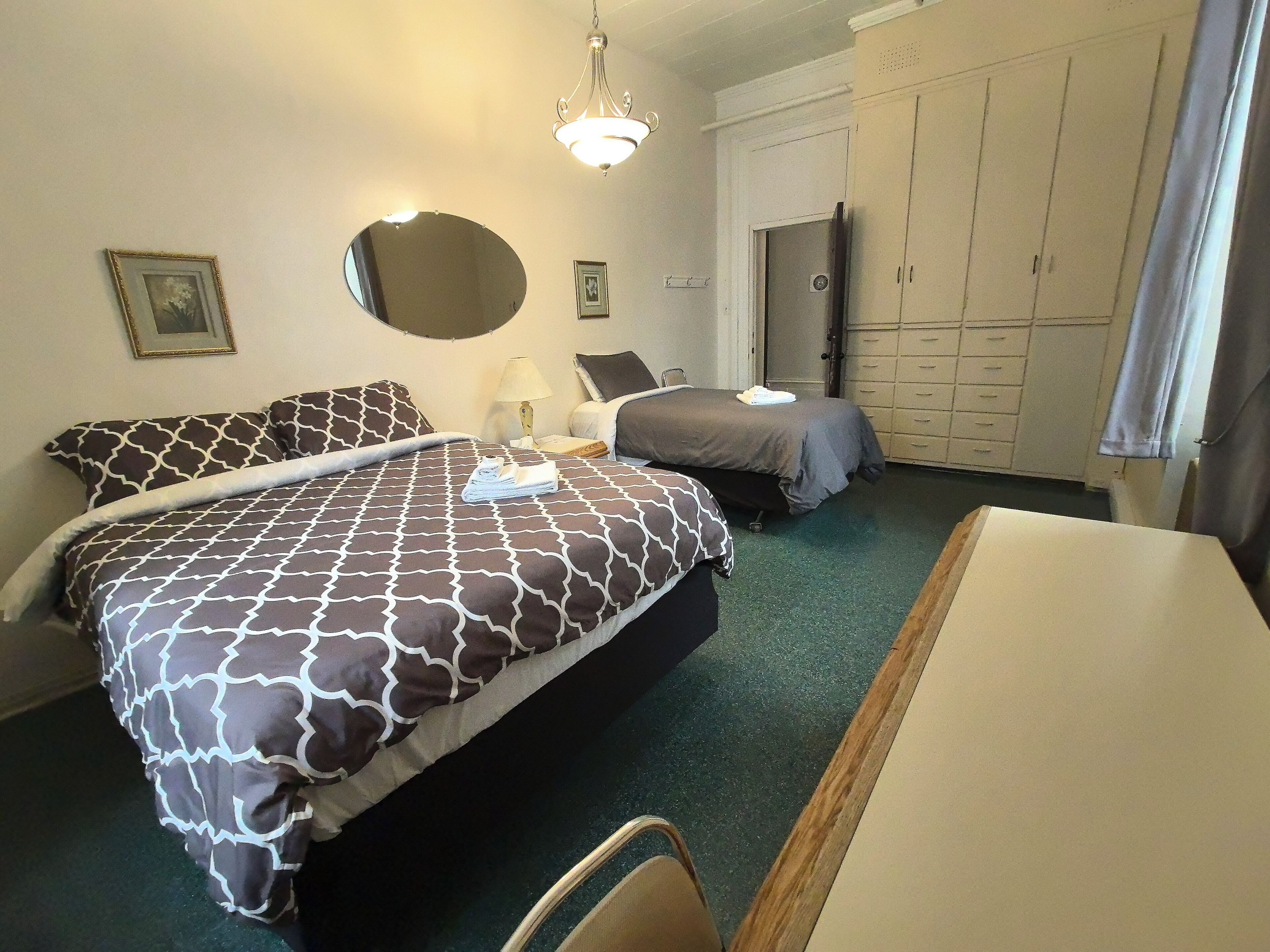 Une chambre d’hôtel avec deux lits, un bureau, une chaise, une armoire et un miroir.