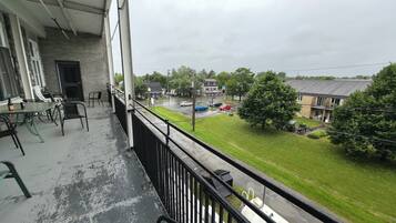 A balcony with a view of a residential street, a grassy area, and a building with a brick facade.
