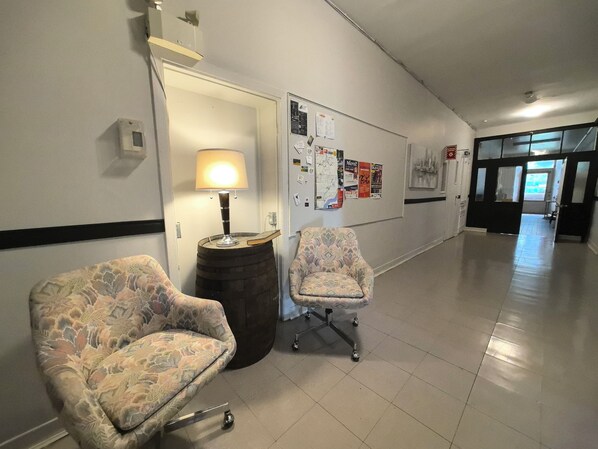 A hallway with two patterned armchairs, a lamp on a barrel, and a bulletin board with various notices. - Auberge du Couvent (Saint-Casimir)