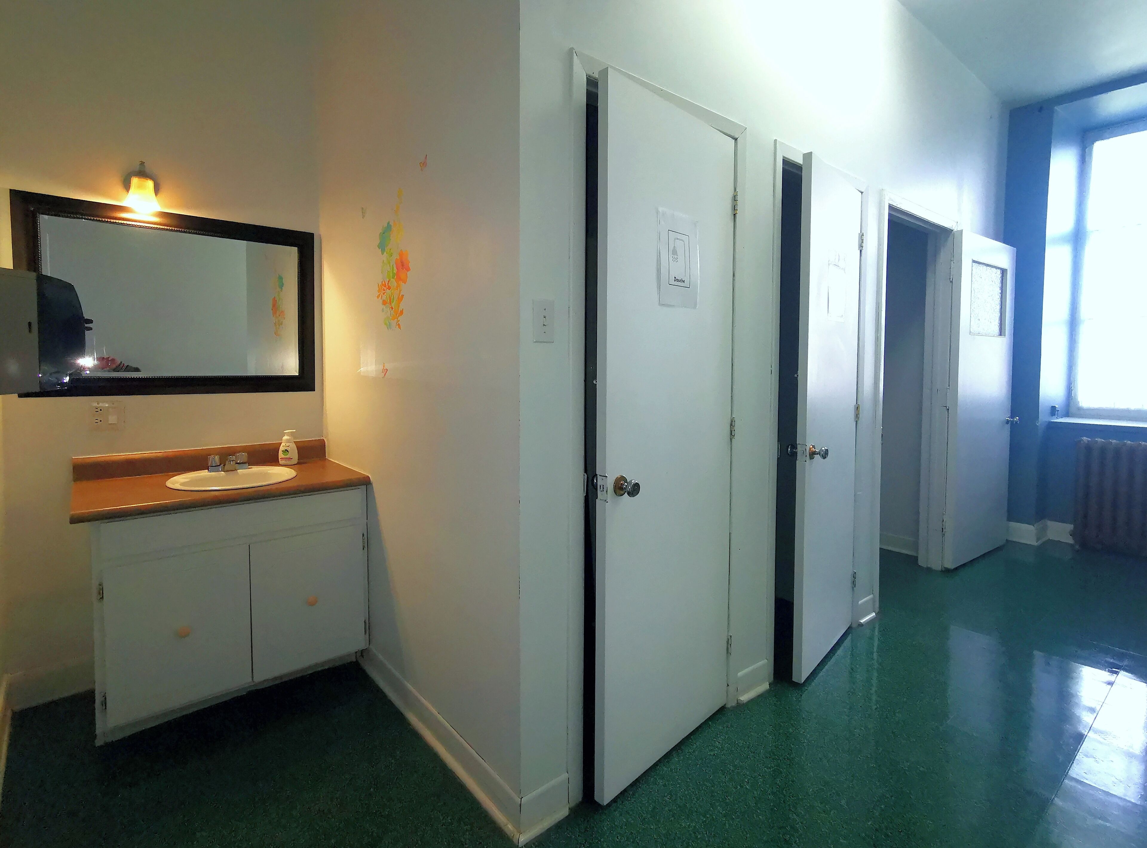 Habitación de hotel con baño que incluye un lavamanos, un espejo y armarios. Hay tres puertas que dan a otras habitaciones.