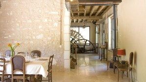 Un espace repas agrémenté d’un mur en pierre, de poutres en bois et d’un escalier menant à une autre pièce.