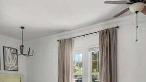 A bedroom with a bed, a white sofa, a glass coffee table, a chandelier, and a ceiling fan. - This adorable studio in The Villages of South Walton is tastefully decorated! (Seacrest)
