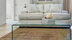 A living room with a beige sofa, a glass coffee table, and a woven rug. - This adorable studio in The Villages of South Walton is tastefully decorated! (Seacrest)