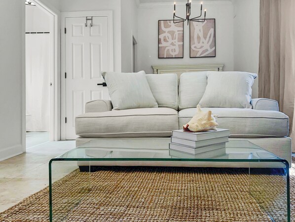 A living room with a beige sofa, a glass coffee table, and a woven rug.