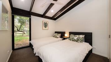 A bedroom with two beds, a ceiling fan, a window with a view of greenery, and a framed plant on the wall.