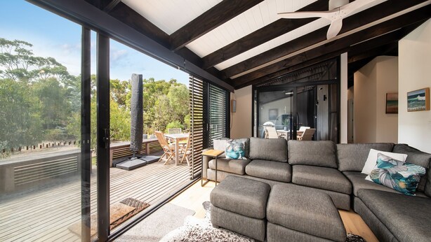 En moderne stue med en stor grå hjørnesofa, træterrasse og glasdør til et udendørs område.