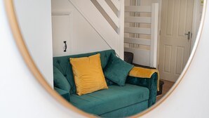 En turkis sofa med et sennepsfarvet tæppe og puder, placeret i et rum med en hvid dør og en trappe i baggrunden.