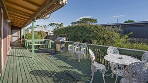 Une terrasse en bois avec une rambarde verte, des meubles d’extérieur blancs et un barbecue.