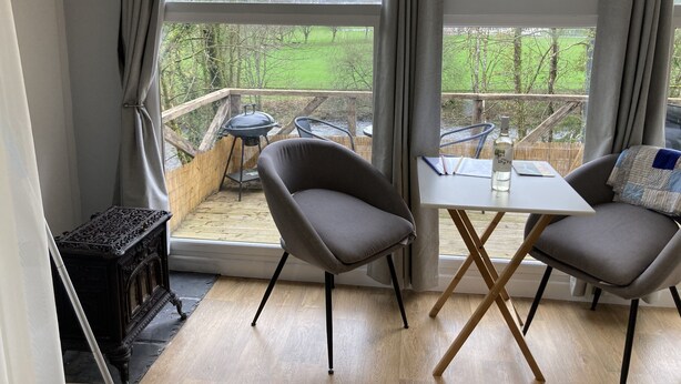 Ein gemütliches Zimmer mit Blick auf eine grüne Landschaft, ein Tisch mit Stühlen und ein kleiner Holztisch mit einer Flasche.