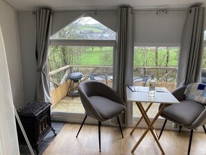 A cozy room with a view of a green landscape, a table with chairs, and a small wooden table with a bottle. - Riverside Retreat Relaxing beautiful surrounding set in 3 acres and pet friendly (Llandysul)