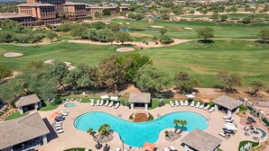 Un complexe hôtelier doté d’une grande piscine, de plusieurs espaces de détente et d’un terrain de golf en arrière-plan.