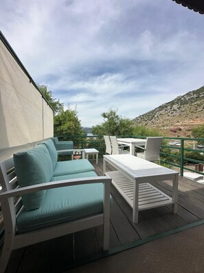 An outdoor patio with a sofa, table, and chairs, overlooking a hilly landscape.