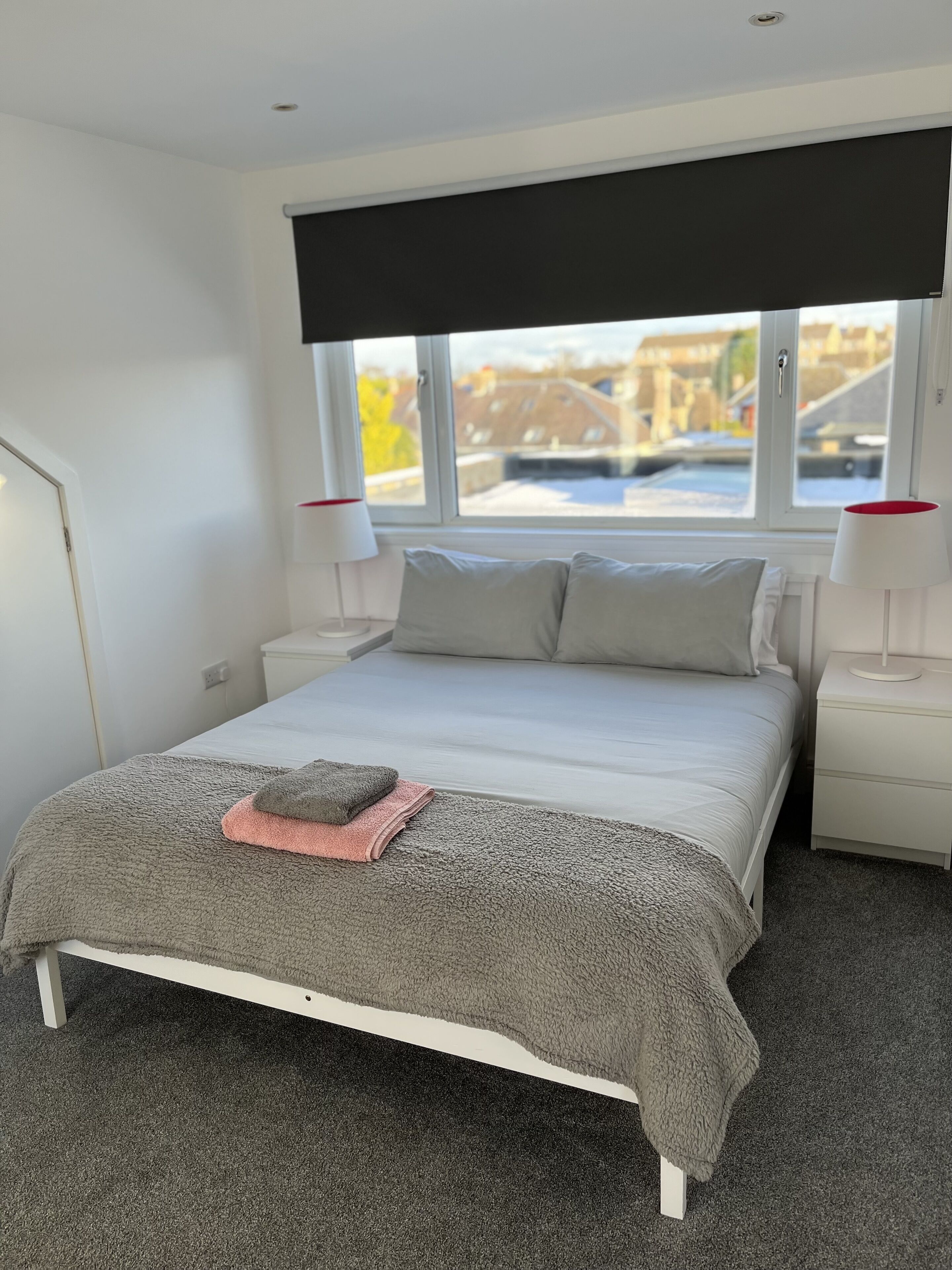 A modern bedroom with a large bed, two bedside tables, a window with a view of the outside, and a ceiling light.