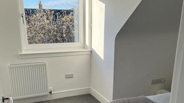 A bedroom with a window, radiator, and a bed with a grey and pink blanket. - Perfect 4 bedroom two bathroom home (Edinburgh)