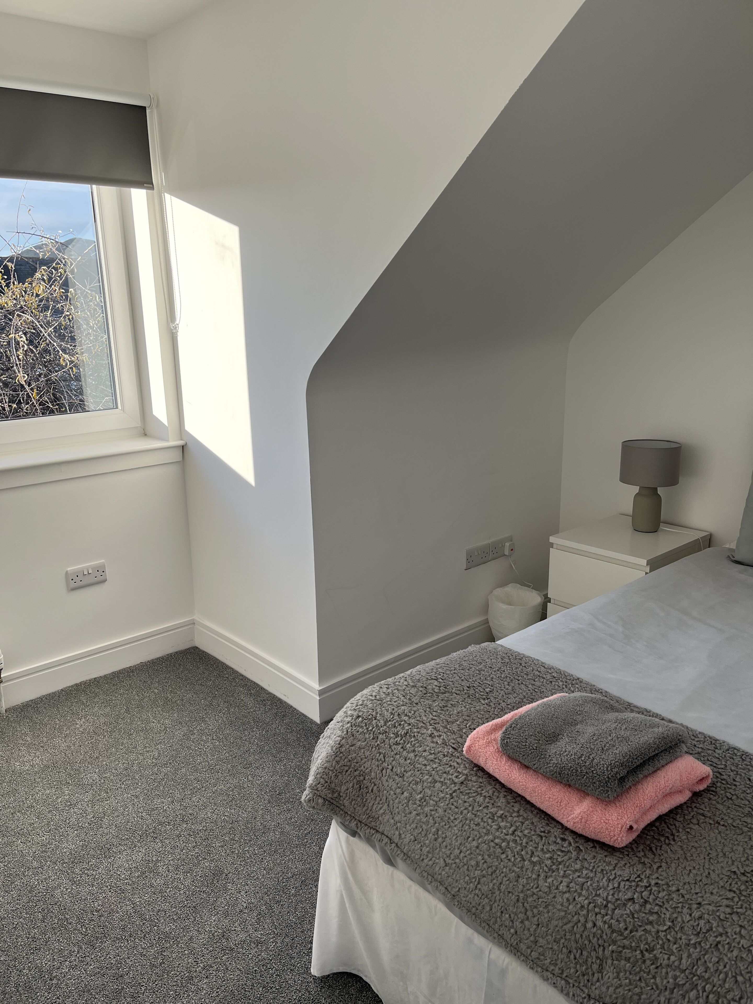 A bedroom with a bed, a nightstand, a lamp, and a window with a view of trees.