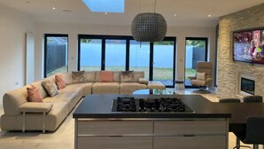 A modern living room with a large sofa, a kitchen island with a stove, and a fireplace.