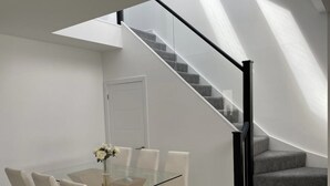 A modern interior with a glass-top dining table, white chairs, a vase with flowers, and a staircase with grey carpet and black railings.