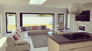 A modern living room with a L-shaped sofa, a kitchen island, and a large window. - Perfect 4 bedroom two bathroom home (Edinburgh)