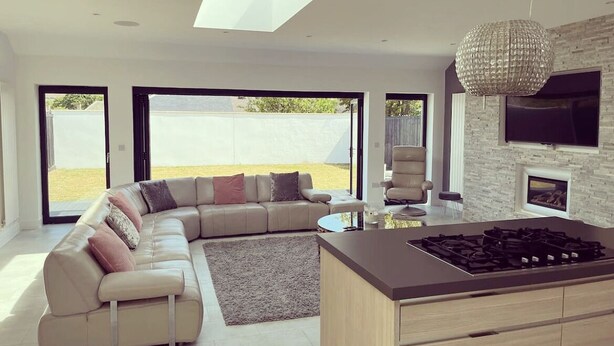 A modern living room with a L-shaped sofa, a kitchen island, and a large window.