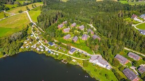 Ilmakuva järvenrantaisesta asuinalueesta, jossa on taloja, suuri rakennus ja tie.