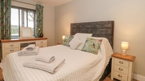 Un lit bien fait, recouvert d’une couette blanche, avec deux oreillers et des serviettes pliées posées sur une table de chevet en bois.