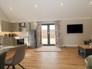 A modern kitchen with a dining area, a flat-screen TV mounted on the wall, and a view through the glass door. - Little Haven (Blandford Forum)