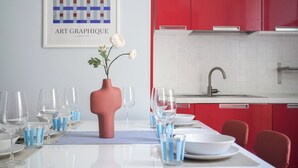 A modern dining area with a white table set for a meal, a pink vase with flowers, and a kitchen with red cabinets in the background. - Apartment for 9 people - 4 min walk from Mestre Station (Venice) (Venezia)