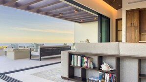 Una sala de estar moderna con un gran ventanal con vista al océano, un sofá, una mesa de centro y una estantería.