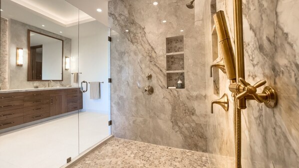A modern bathroom with a glass shower enclosure, marble walls, and a gold showerhead.