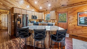 A wooden cabin interior with a kitchen featuring a large island, bar stools, and built-in appliances. - Near PF & Dollywood! 4 BD Retreat-Theater-Arcades-Hot Tub-Fire Pit-Pool Table (Sevierville)