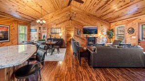 A cozy cabin interior with a wooden ceiling, a dining area with a marble table, a sofa, and a fireplace. - Near PF & Dollywood! 4 BD Retreat-Theater-Arcades-Hot Tub-Fire Pit-Pool Table (Sevierville)