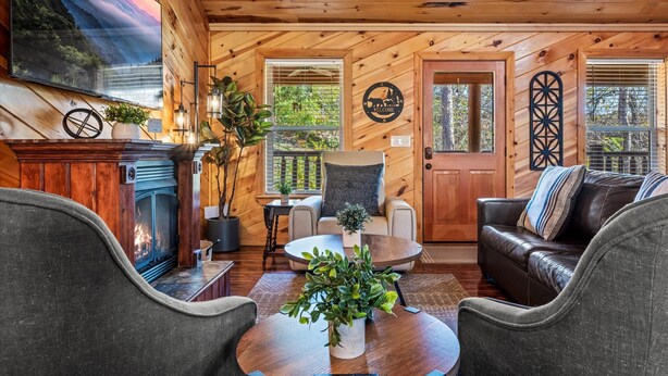 A cozy cabin interior with a fireplace, comfortable seating, and a large TV mounted on the wall. - Near PF & Dollywood! 4 BD Retreat-Theater-Arcades-Hot Tub-Fire Pit-Pool Table (Sevierville)