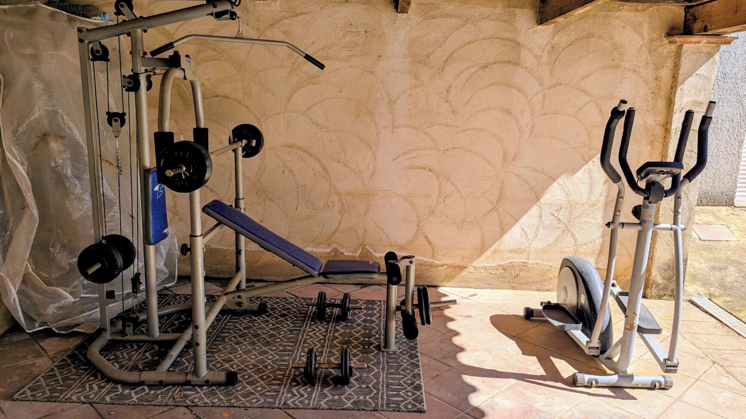 Un gimnasio en casa con una prensa de banca, un soporte para pesas y una máquina elíptica.
